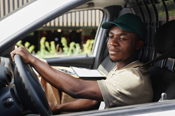 Side view portrait of young black man driving delivery truck and wearing uniform