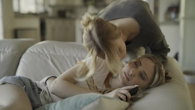 Slow motion of girl kissing sister laying on sofa watching television / Highland, Utah, United States