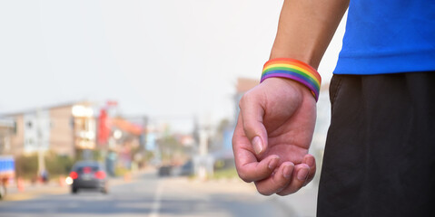 Rainbow wristband on right hand, blurr street background, concept for lgbtq+ genders celebrations, gender self confidence and calling all people to respect human rights in pride month.