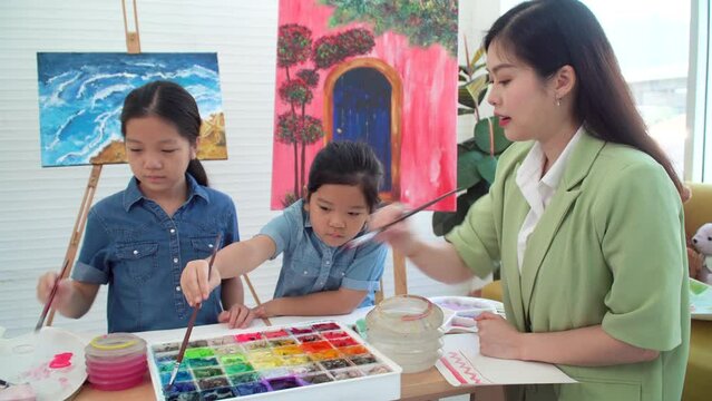 Asian two siblings learning study watercolor paint together at home. Teacher or parent teach student or daughter drawing paint color imagination on paper homework.Activity creativity education concept