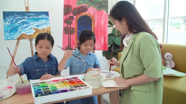 Asian two siblings learning study watercolor paint together at home. Teacher or parent teach student or daughter drawing paint color imagination on paper homework.Activity creativity education concept