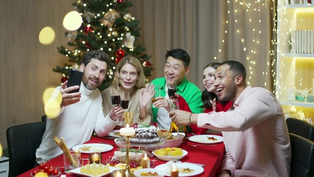 friends celebrating Christmas Eve, chatting on a video call online using a mobile phone by decorated table, taking picture. conference chat on holiday party. Happy People meeting celebrating new year