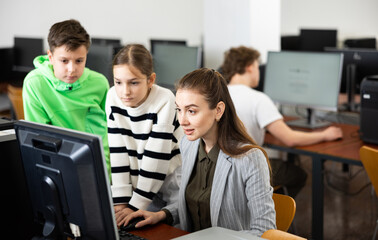 Fototapeta premium Interested teenagers studying with young female teacher in information technology class at college, sitting around one computer