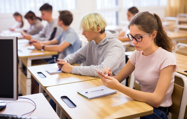 Confident teen students using social media on phones while studying in high school