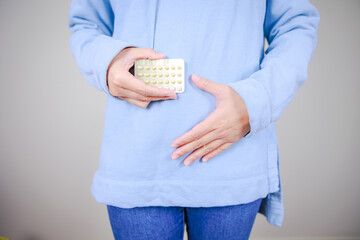 経口避妊薬（低用量ピル）を持ちお腹をさする女性	