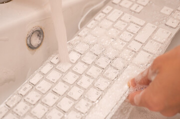 Woman washing white computer keyboard with a sponge with foam.