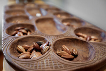 A hand carved Pallanguzhi game board contains seeds which are used as game pieces.