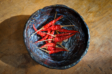 A bowl of red Thai Chili Peppers is seen from above on an old wooden table.