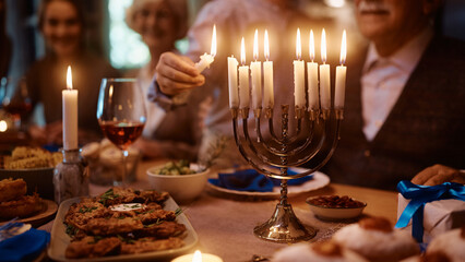 Close up of boy lights candles in menorah while celebrating Hanukkah with his family at dining table.