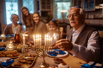 Close up of senior Jewish man lights menorah during family dinner on Hanukkah.