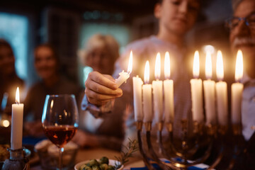 Close up of Jewish kid lights menorah during family dinner on Hanukkah.