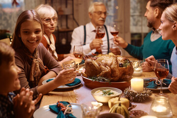 Happy teenage girl and her family enjoying in conversation during Thanksgiving dinner at dining table.