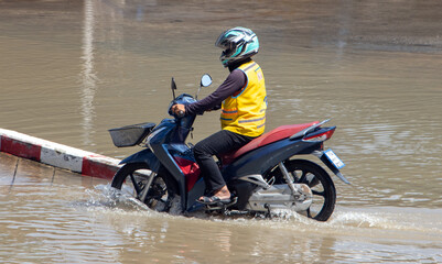  A taxi driver on a motorcycle drives through a flooded street, Thailand