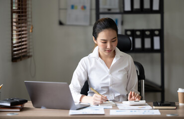 Cute asian woman having a cup of tea while using laptop computer in office