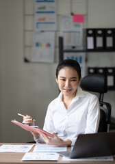 Cute asian woman having a cup of tea while using laptop computer in office