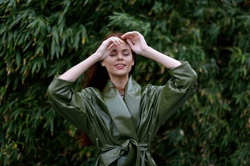 Woman with a beautiful smile posing against the green bamboo in spring, red flying hair in the windy weather, the concept of style and fashion 