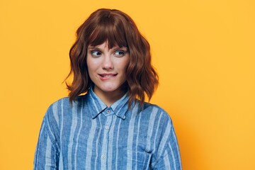 a happy, thoughtful woman stands on a yellow background in a blue shirt and thoughtfully bites her lower lip looking away