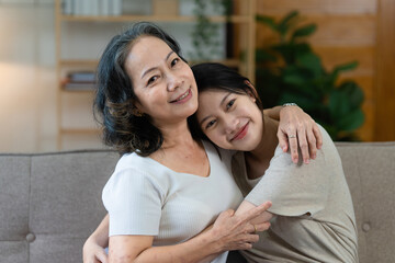 Happy senior Asian woman and her adult daughter are cuddling on the couch