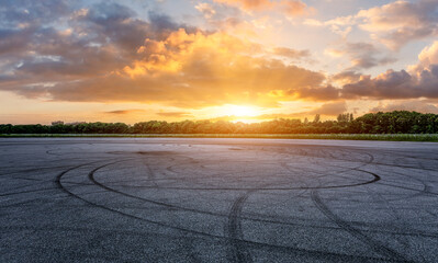 Empty asphalt race track road and green forest with sky clouds at sunset