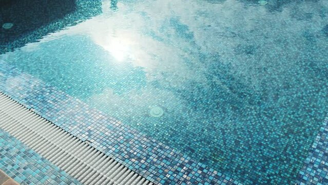 Sun glare in a beautiful swimming pool lined with blue mosaics. Clear blue water in the pool. Relax in the backyard of a country house
