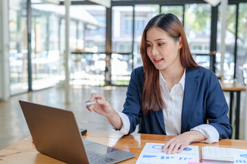 Portrait of smiling Asian business woman enjoying work ideas sitting on laptop at office.