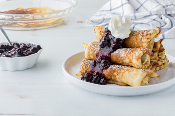A pile of crepes topped with fresh homemade blueberry sauce and whip cream.