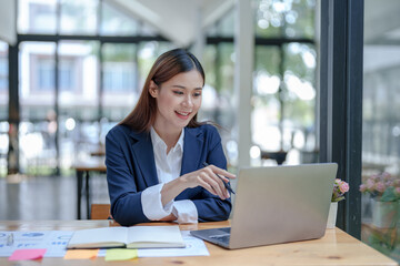 Portrait of smiling Asian business woman enjoying work ideas sitting on laptop at office.