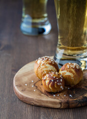 Three homemade pretzel nuggets on a wooden board with beers in behind.