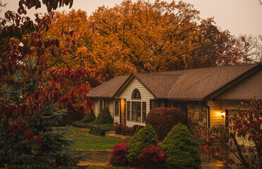 View of suburban Midwestern house on rainy autumn day; colorful trees in front yard and background; view from the street