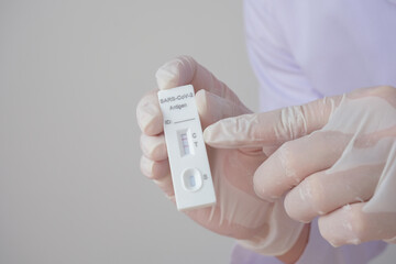 A doctor or nurse wearing rubber gloves is holding a positive Antigen Rapid Test kit (ATK) with two red lines. During a swab test for COVID-19