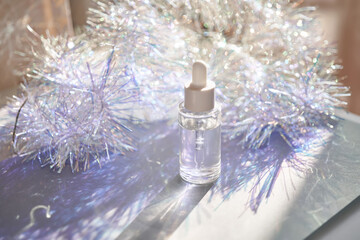 A bottle of serum with a pipette in tinsel in a Christmas theme in purple shades.