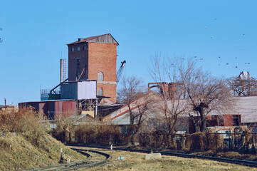 Fototapeta na wymiar Old industrial buildings next to railroad tracks on an autumn morning. Red brick tower. Pigeons in the blue sky without clouds. No people. Copy space