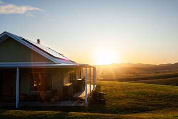 Homestead on hilltop with last rays of sunlight shining over scene and solar panels on roof