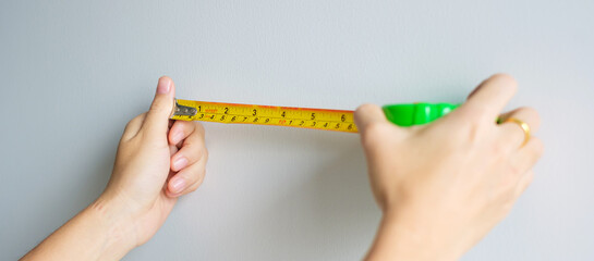 Man hand using tape measure for measuring with wall backgrounds at home. DIY, Interior design,...
