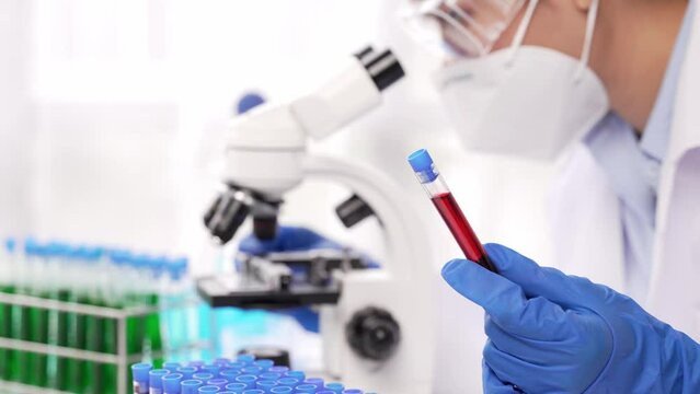 Doctor hand taking a blood sample tube from a rack with machines of analysis in the lab background, Technician holding blood tube test in the research laboratory.