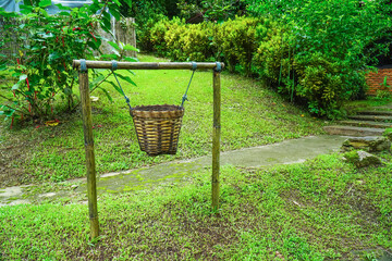 Hanging garbage bin with string beside the street background. Hanging weave wood trash can with tied pole beside footpath