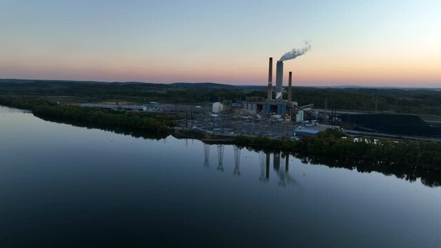 Aerial of electric power plant. Electricity generation. Smokestack factory reflection in water. Power lines. Aerial at sunset.