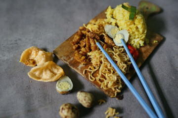 traditional Indonesian food, yellow rice with various side dishes on a cutting board on concrete background