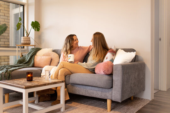 Female same sex couple  in the living room, talking and cuddling on the grey sofa