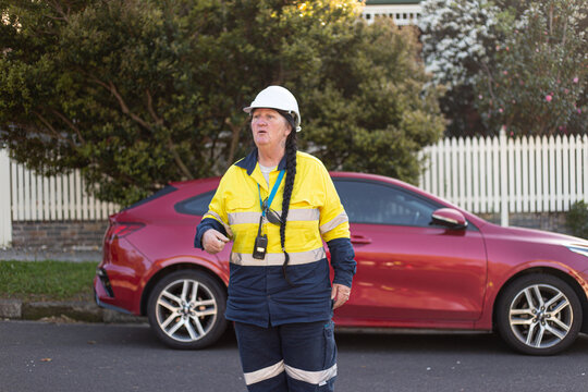 Woman road worker looking away in front of a red car