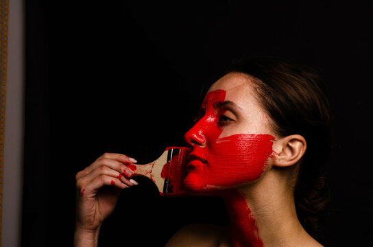 Creative Portrait Of A Young Girl. The Face Is Painted With Red Glitter Paint. The Triangle Is Drawn On The Face. Model In Profile On Black Background