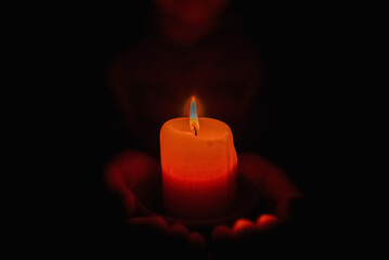 Little boy holding red burning candle in the darkness.Selective focus.Closeup.