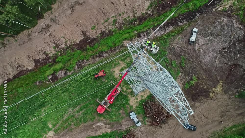 Poster drone overhead view directly above a tall pylon. construction workers in basket high up on wires.