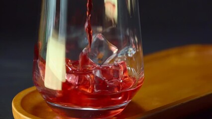 Pouring red liquid into transparent glass cup with ice cubes. Wine, fruit juice, herbal tea abstract, slow motion - Powered by Adobe