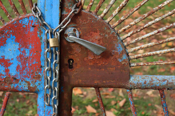 Close-up of blue and rusty old gates of are locked with chain and padlock around them.  Locked...