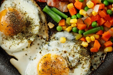 Fried eggs with vegetables in a pan.