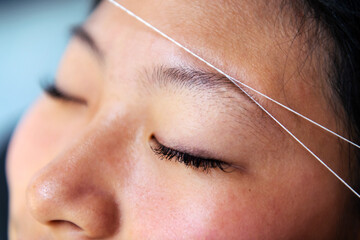 detail of an eyebrow waxing with threading on a young woman in a beauty salon, concept of wellness...