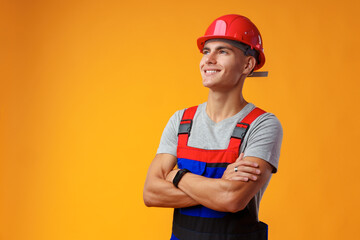 Young construction worker in helmet and uniform posing on yellow background in studio