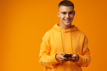 Portrait of a smiling young man holding mobile phone on yellow background