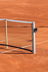 Baseline and net of an empty clay tennis court on a sunny day